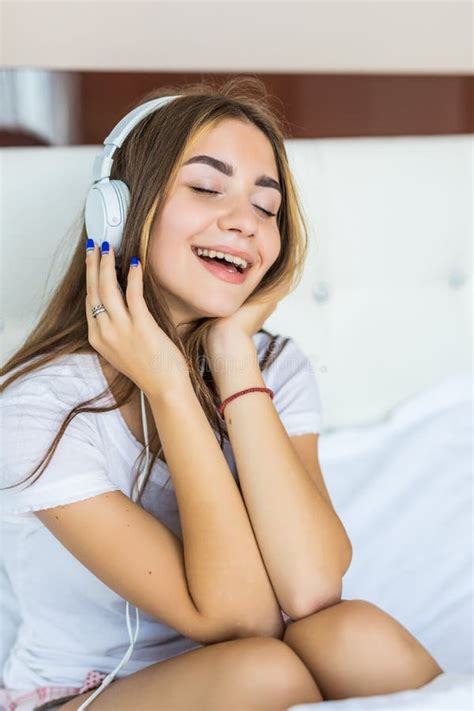 Young Pretty Woman Listening To Music In Headphones On Bed Stock Photo