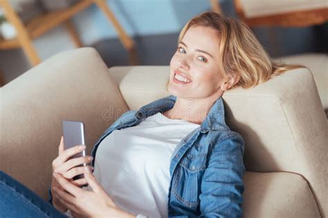 smiling cheerful woman holding a phone while resting on a sofa stock image image of delighted