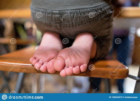 Child is Sitting on Chair in Room. Legs and Feet of Kids Stock Image
