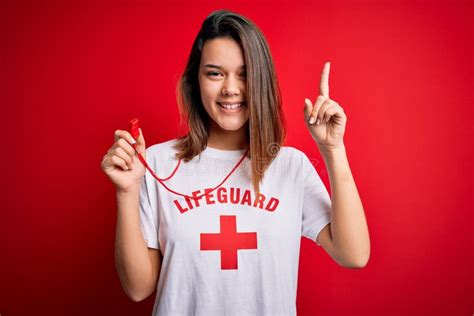 Young Beautiful Brunette Lifeguard Girl Wearing T Shirt With Red Cross Using Whistle Pointing