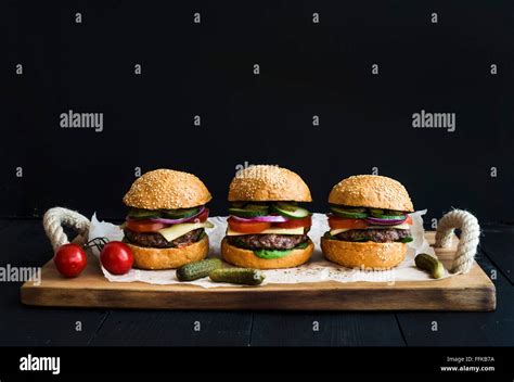 Fresh Homemade Burgers On Wooden Serving Board Over Black Background