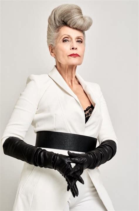 an older woman wearing black gloves and a white coat with her hands on her hips