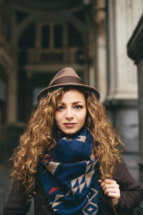 portrait of beautiful woman with hat and curly hair in urban environment by stocksy