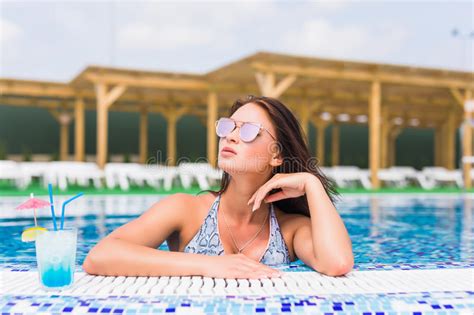 Tenned Beautiful Woman In Blue Bikini And Sunlasses Sitting In Swimming Pool With Cocktail