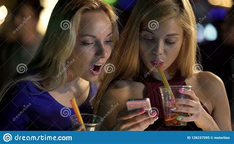 Pretty Girls Drinking Cocktails At Bar Checking Social Networks On Smartphone Stock Image