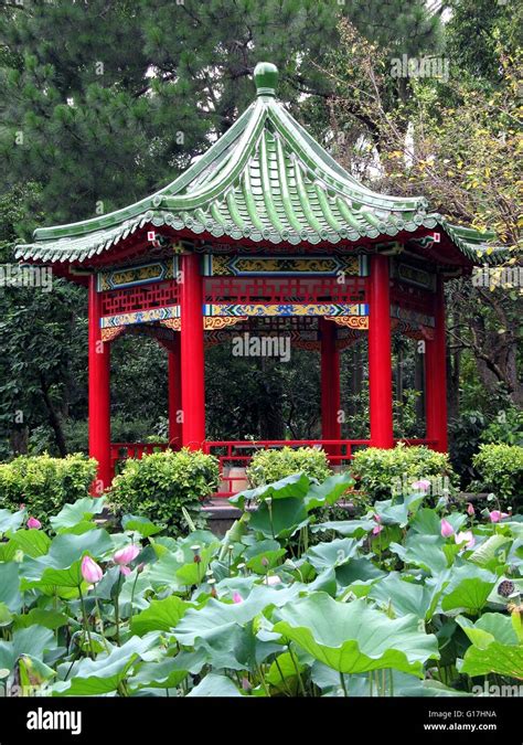 A Chinese Pavilion With Red Columns And Green Roof Amidst A Pond With