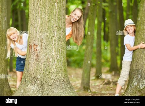 Mother And Two Kids Have Fun Playing Hide And Seek In The Forest Stock