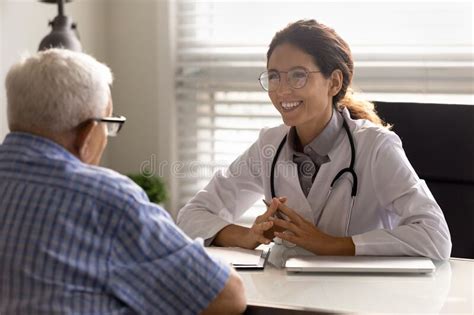 Happy Young Doctor And Senior Patient Talking In Hospital Stock Photo