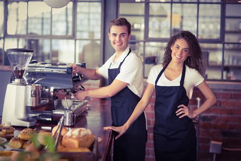 Portrait Of Smiling Waitress In Front Of Colleague Making Coffee At