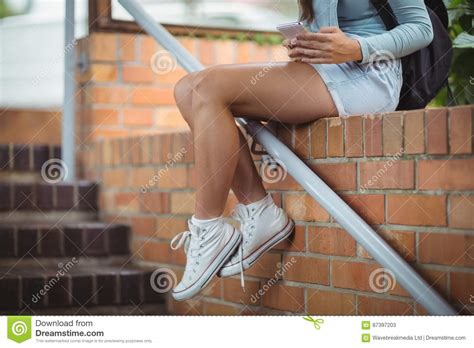 Schoolgirl Sitting On Brick Wall And Using Mobile Phone Stock Image