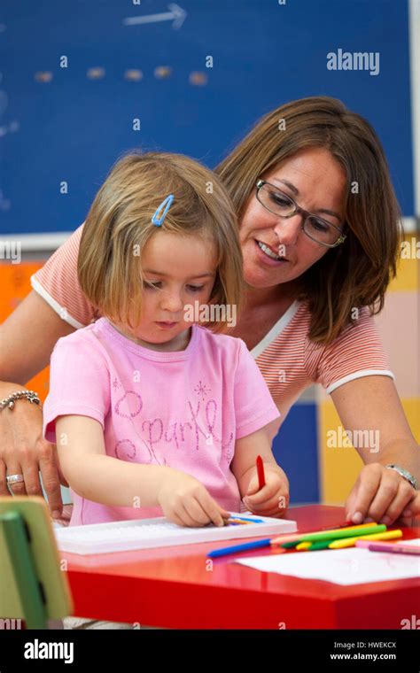 Preschool Girl And Teacher With Colouring Pens In Classroom Stock Photo