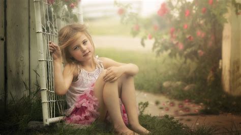 Cute Little Girl Is Sitting On Grass Leaning Back On Gate Wearing White