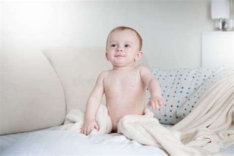 Smiling Baby Boy In Diapers Sitting On Bed With White Sheets Stock