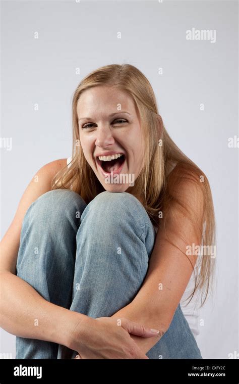 lovely blond woman sitting on a wooden stool with her knee raised up near her chin looking at