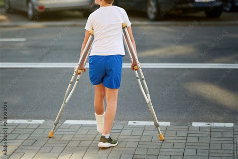Young Boy In Orthopedic Cast On Crutches Walking On The Street Near The