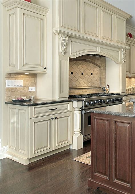 A modern glass and stainless steel range hood hanging over the kitchen island is softened by a wall of reclaimed wood leading down to the floor. PRASADA Antique white kitchen with large decorative range ...