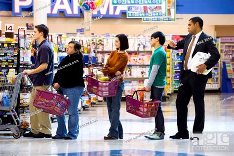 People Waiting In Line With Shopping Baskets At Grocery Store Stock