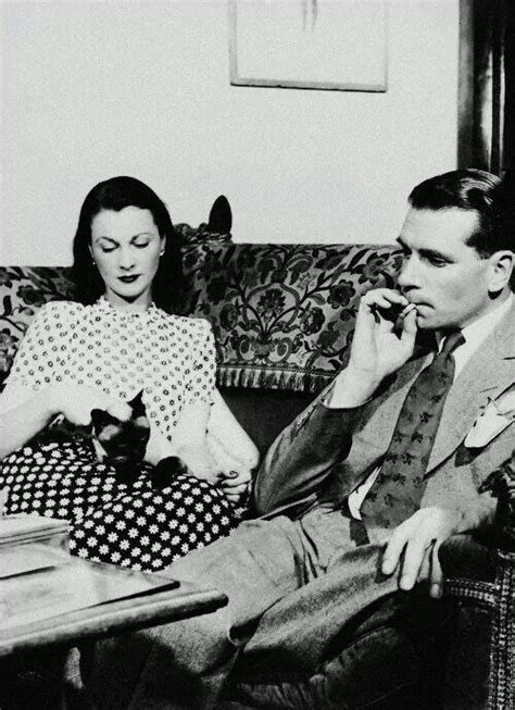 A Man And Woman Sitting On A Couch Talking On Cell Phones