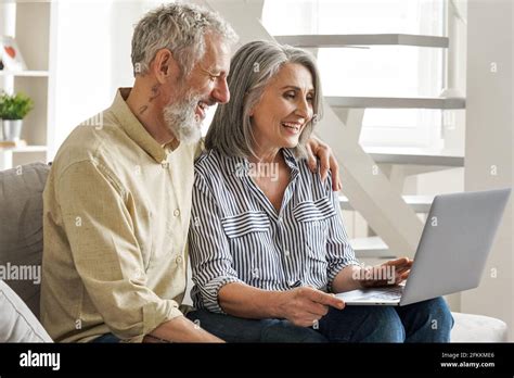 Happy Older Middle Age Couple Using Laptop Looking At Computer Sitting