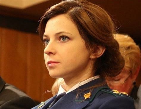 A Woman In Uniform Sitting At A Table With Other People Behind Her Looking Off Into The Distance