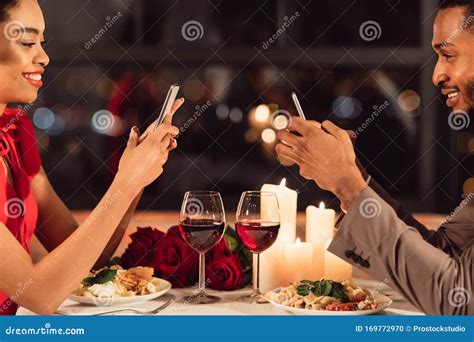 Couple Using Phones During Romantic Dinner Date In Fancy Restaurant