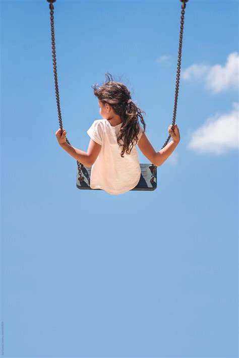 Girl Sitting On A Swing Flying High In The Blue Sky Stocksy United