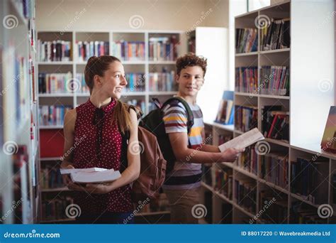 Classmates Interacting While Selecting Book In Library Stock Photo