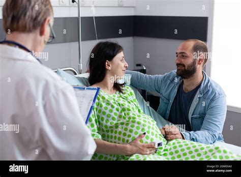 maternity doctor examining pregnant woman sitting in hospital ward bed at medical facility