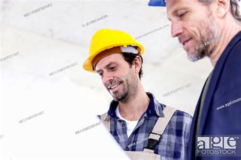 Construction Worker And Architect With Plan Talking On Construction