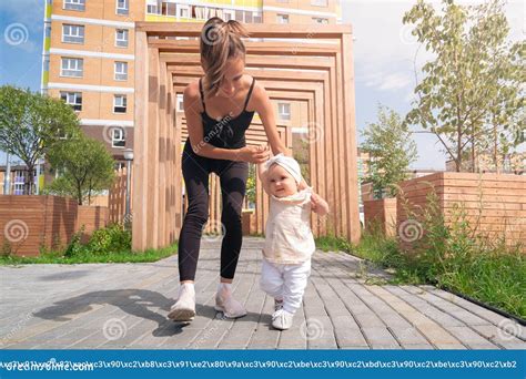 mamá y su hija pequeña caminan en el patio de la ciudad niño aprende a caminar foto de archivo
