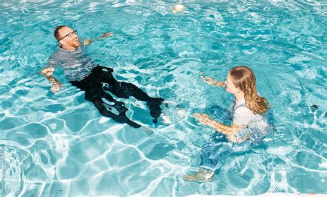 couple laughing while swimming with all their clothes on during spontaneous summer pool party by