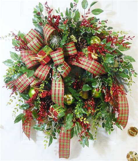 A Christmas Wreath With Red Green And Gold Decorations On It Next To A Bell