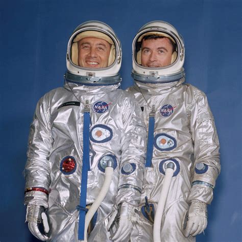 Two Men In Silver Spacesuits Standing Next To Each Other With Their