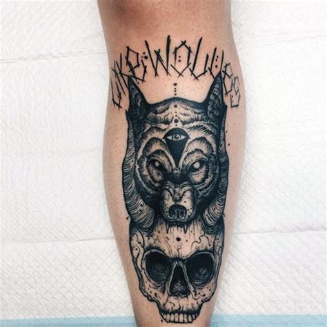 creepy looking black ink leg tattoo of creepy skull with wolf head and lettering tattooimages