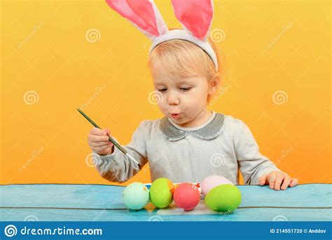 A Small Child With Pink Bunny Ears Paints Easter Eggs For The Holiday