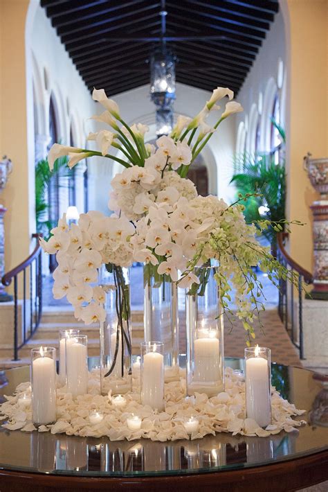 A Centerpiece With Candles And Flowers On A Table In Front Of A