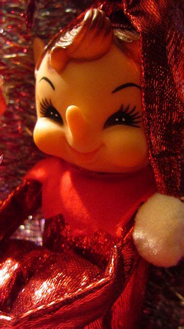A Close Up Of A Toy Doll On A Surface With Red Sequined Material
