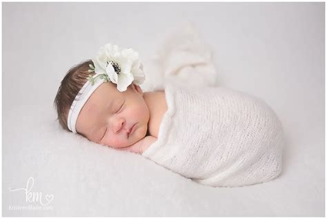 A Baby Is Sleeping With A Flower In Her Hair And Wearing A White Wrap