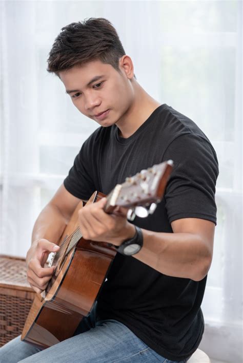 A Man Sitting And Playing Guitar On A Chair Free Photo