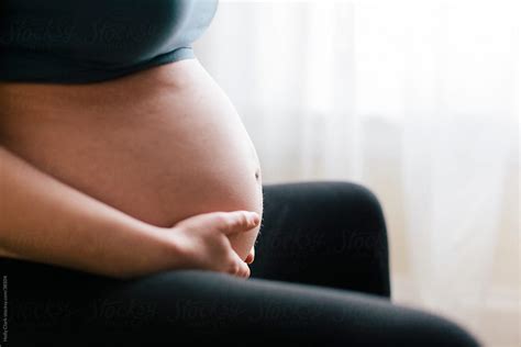 Close Up Of Seated Woman S Pregnant Belly With Hands By Stocksy Contributor Holly Clark