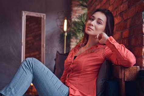 A Charming Brunette In Casual Clothes Sitting In A Room With Lof Stock