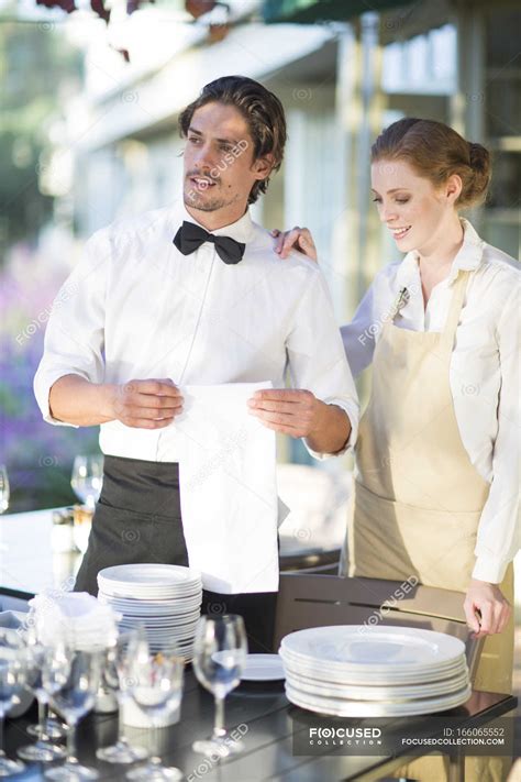 Waiter And Waitress Setting Up Tables In Patio Restaurant Uniform