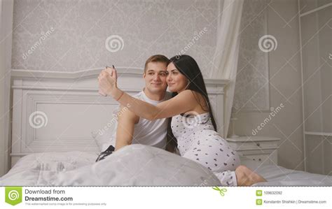 couples affectueux gais heureux faisant le selfie dans le lit le jeune type attirant et la