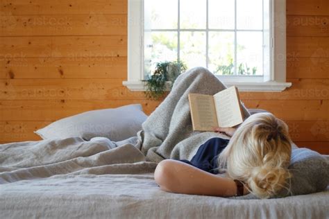 Image Of Woman Lying In Bed Reading Book With Timber Walls And Window