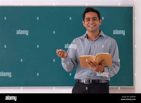 School Teacher Teaching In Front Of Blackboard In Classroom Stock Photo