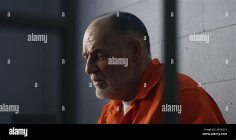 Elderly criminal in orange uniform sits on prison bed and dreams about