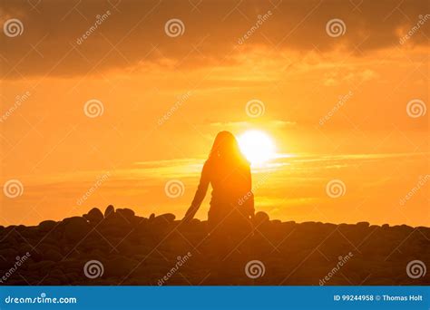 Young Woman Walks Alone Into The Sunset At The Beach Stock Photo