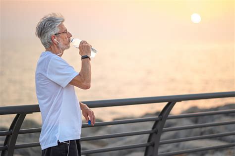 Senior Man Drinking Water During An Exercise Outside By The Seaside At