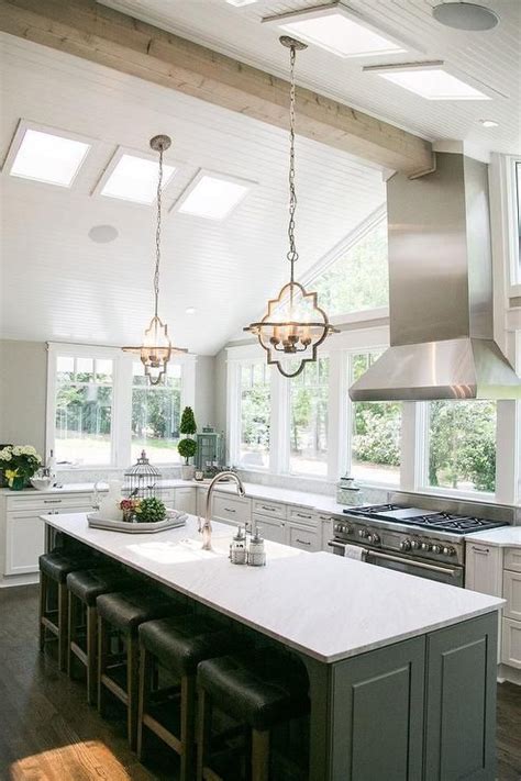 Skylights add valuable natural light and pendant lights add a bit of color. White and gray kitchen features a vaulted ceiling accented ...