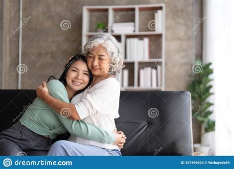 Loving Adult Daughter Hugging Older Mother Standing Behind Couch At